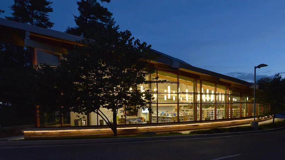 Olney Library at dusk, with illuminated bookshelves visible through its long glass wall.